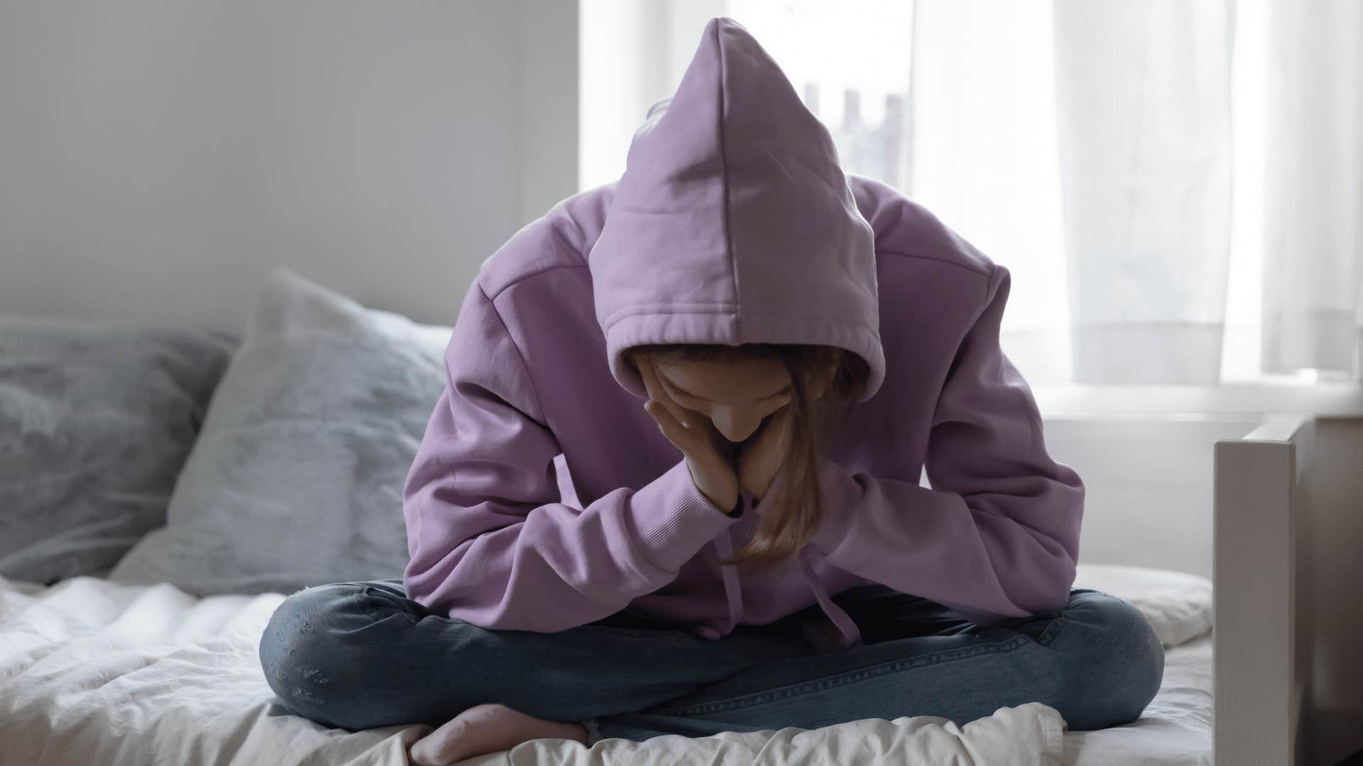 Teenager who was raised with soft parenting covers head with hoodie in her room