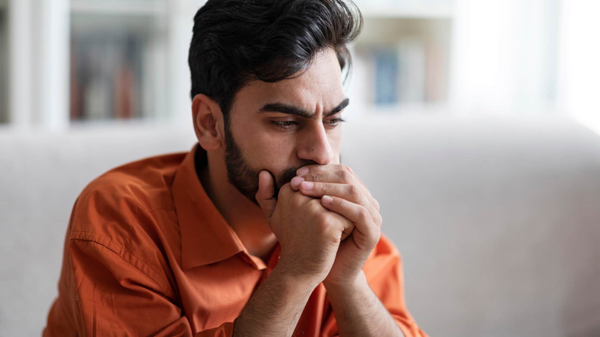 Gen Z man with a beard looking annoyed and sad on a couch 