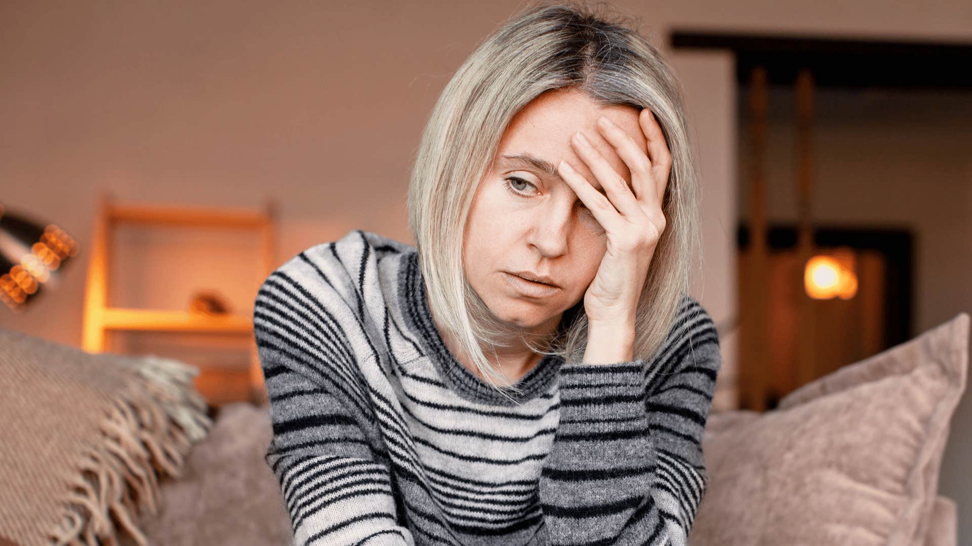 Woman who lives with a controlling man looks ashamed on her couch 