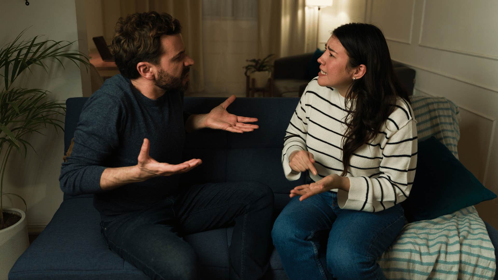 Controlling man looks angry at a very sad woman at home