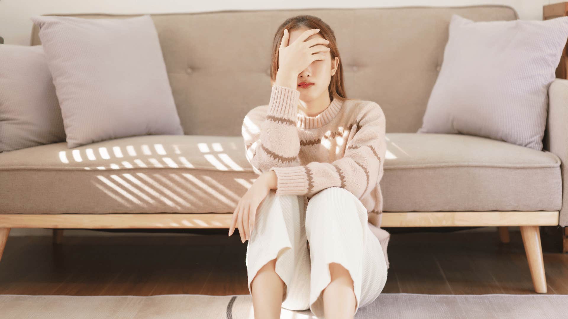 Sad grown daughter sitting by the couch with hand over eyes