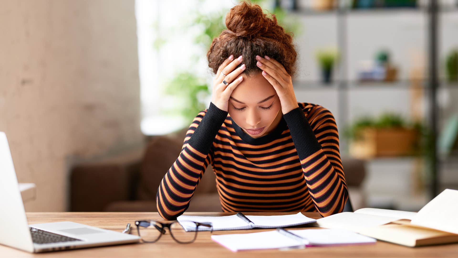 woman in black and orange stripped shirt thinking i'm just tired as she puts head in hand