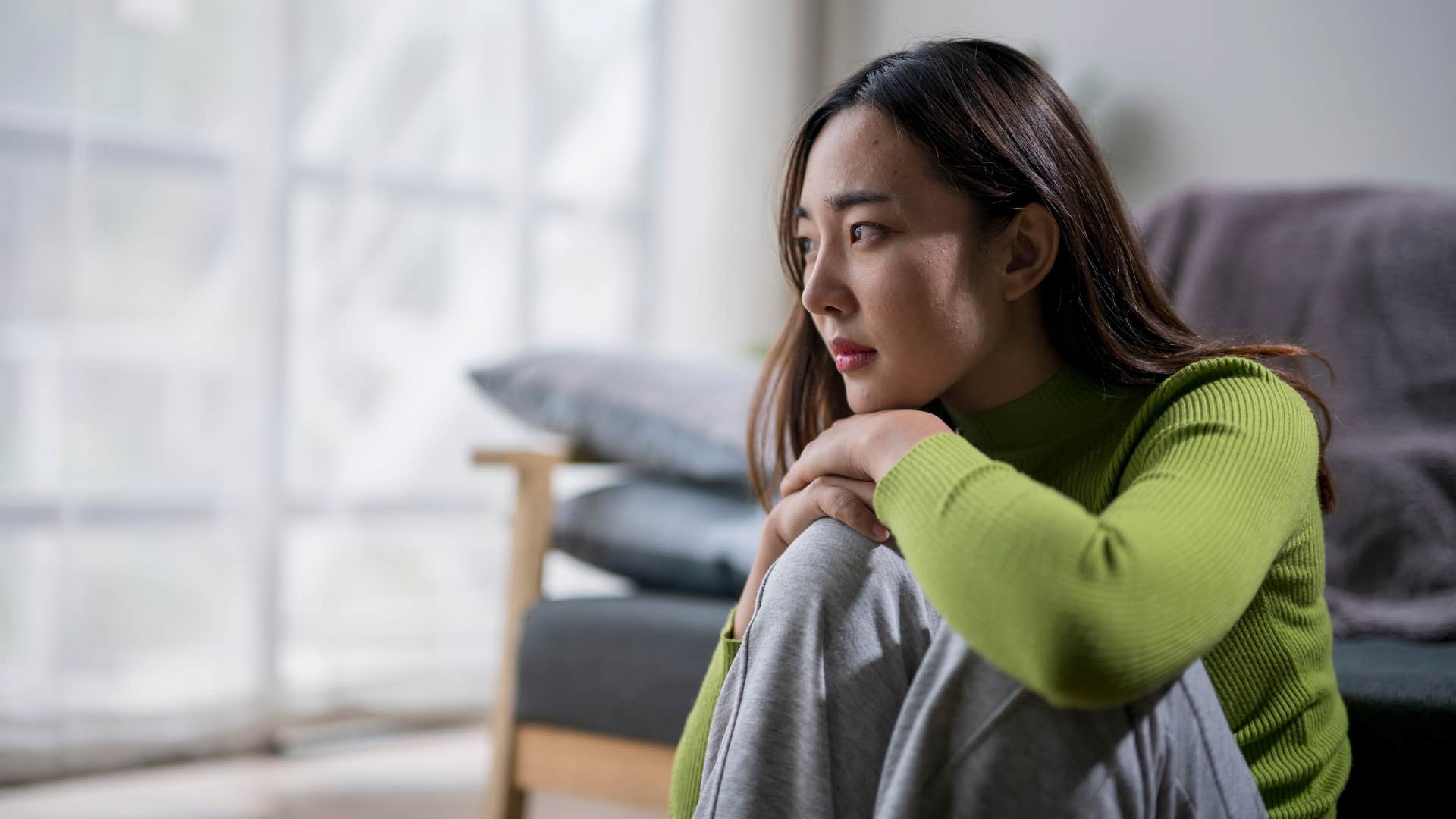 woman in green shirt sitting down clearly upset as she thinks to herself i don't want to burden anyone