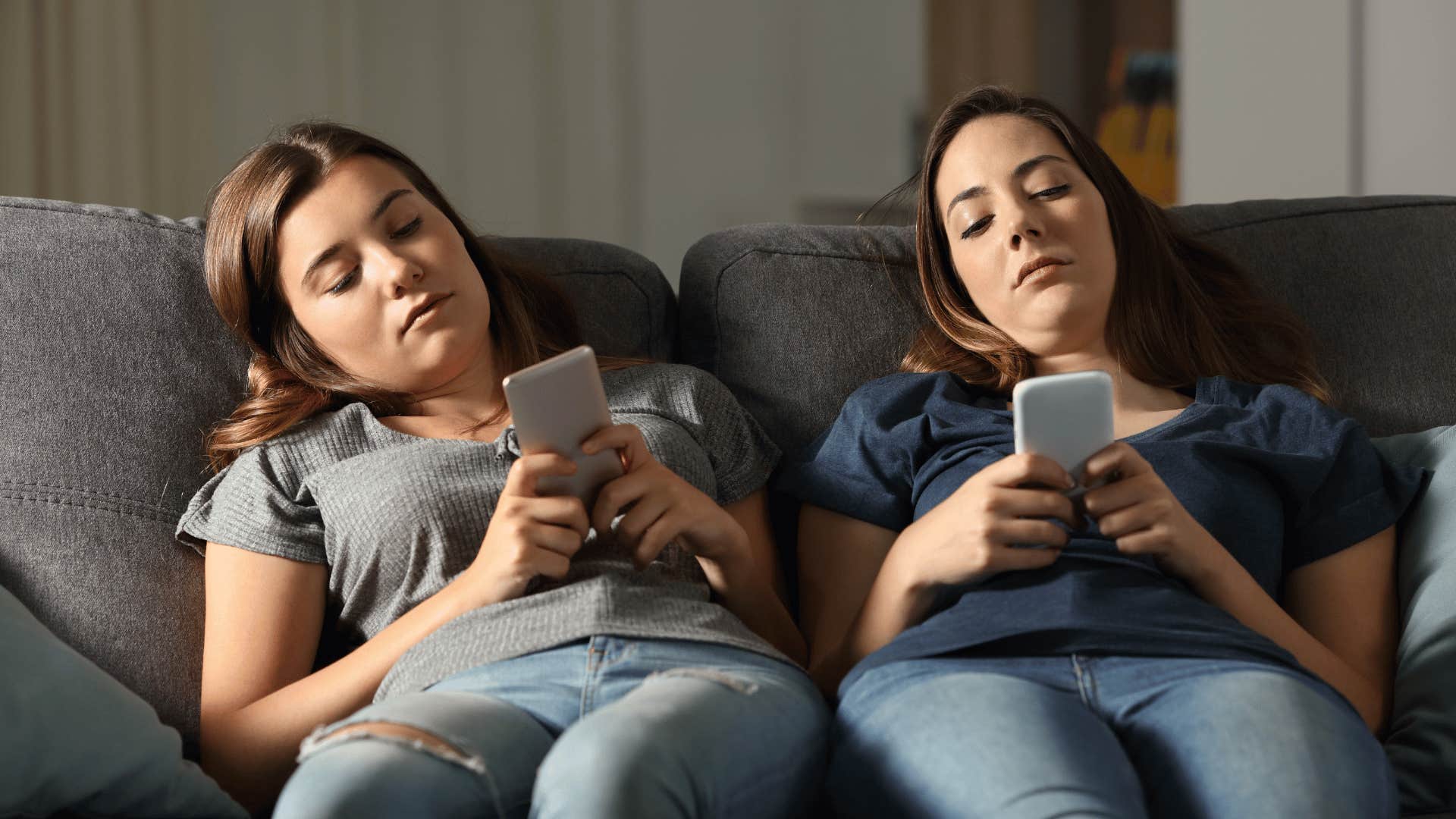 Two young women who are exhausted not lazy using phones on a couch 