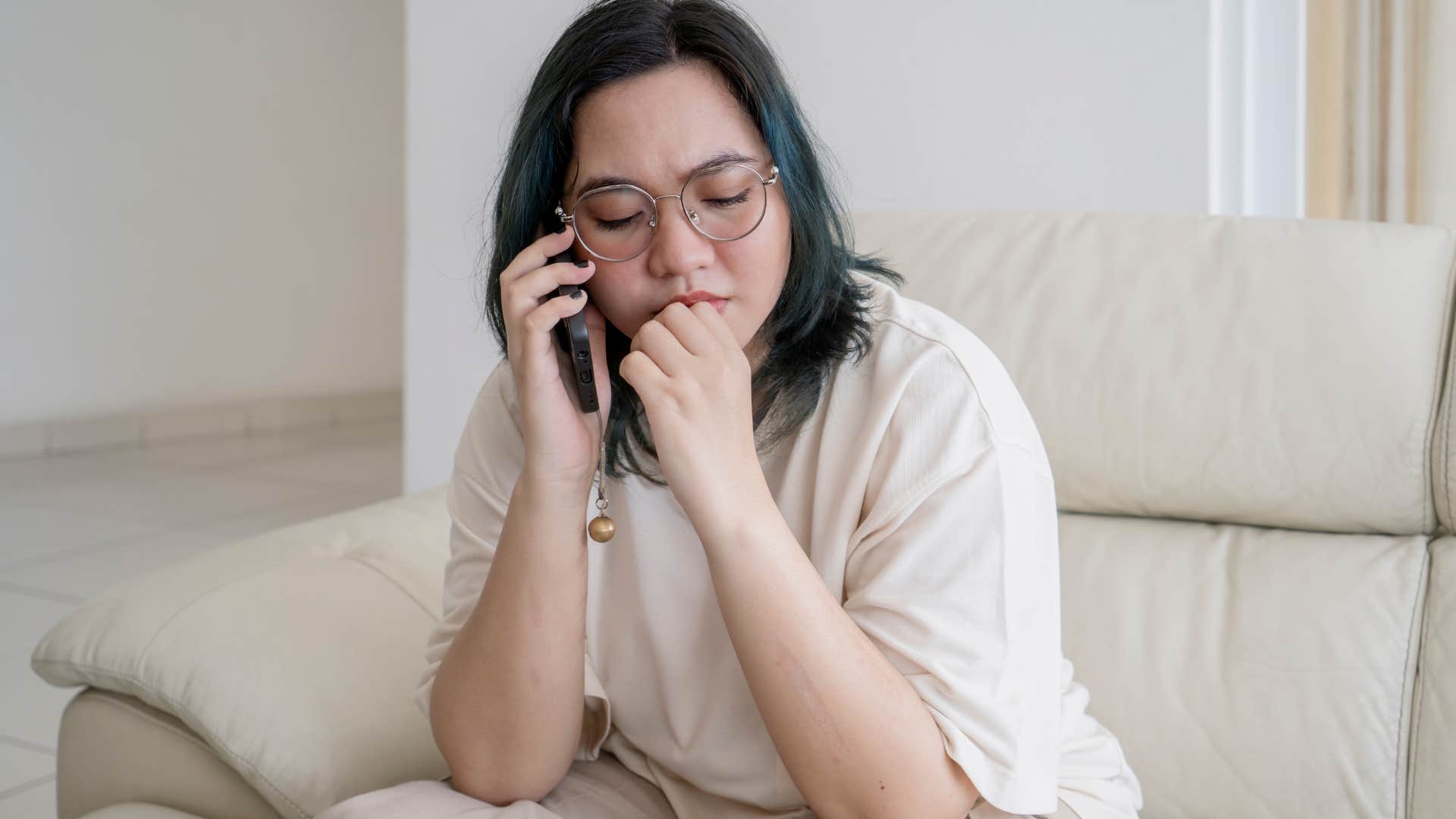 Adult child of divorced parents talks on the phone in a plain room